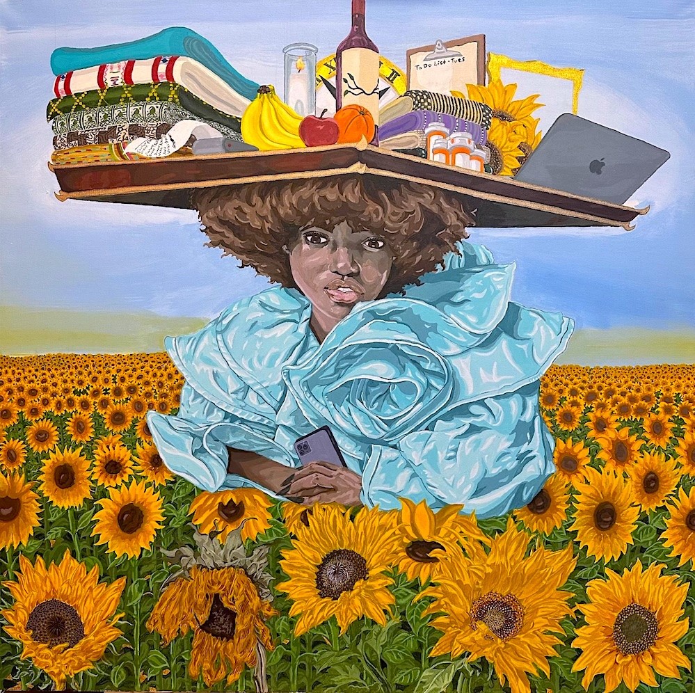 A person with curly hair and a puffy blue outfit stands in a sunflower field. Balanced on their head is a tray holding folded clothes, fruit, medicine bottles, a candle, wine, a laptop, and books. They hold a phone and look forward, surrounded by blooming sunflowers.