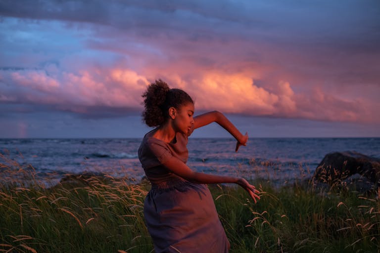 A woman gracefully dances by the sea at sunset, capturing emotion and nature's beauty.